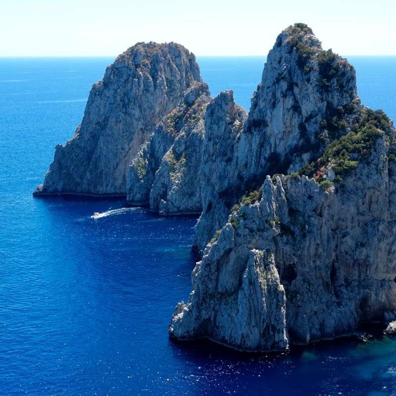 Le formazioni rocciose dei Faraglioni di Capri viste dal sentiero a picco sul mare blu