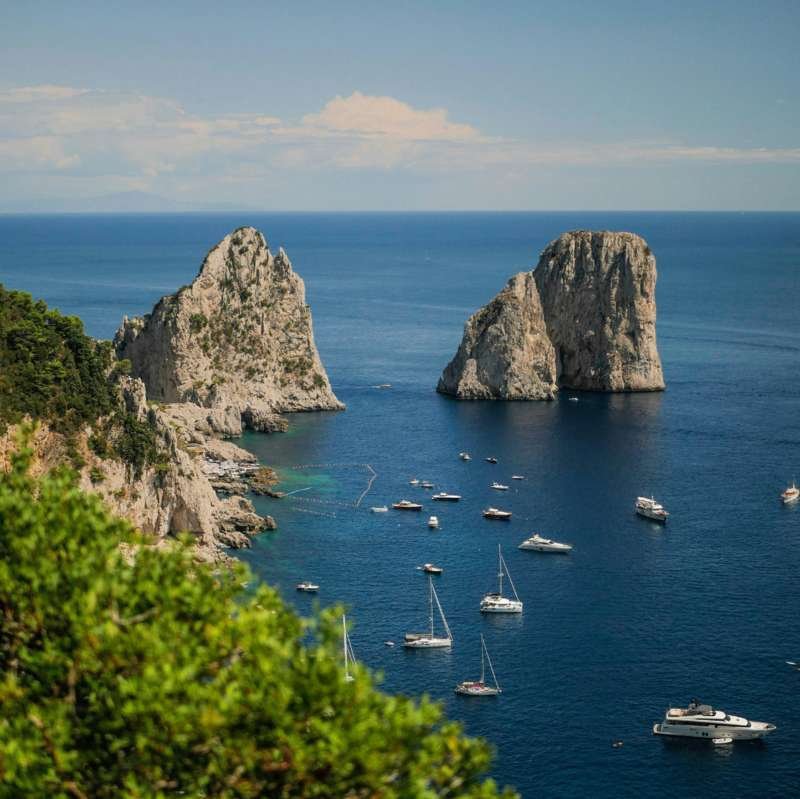 Vista dei Faraglioni e delle barche all'ancora dalle scogliere di Capri
