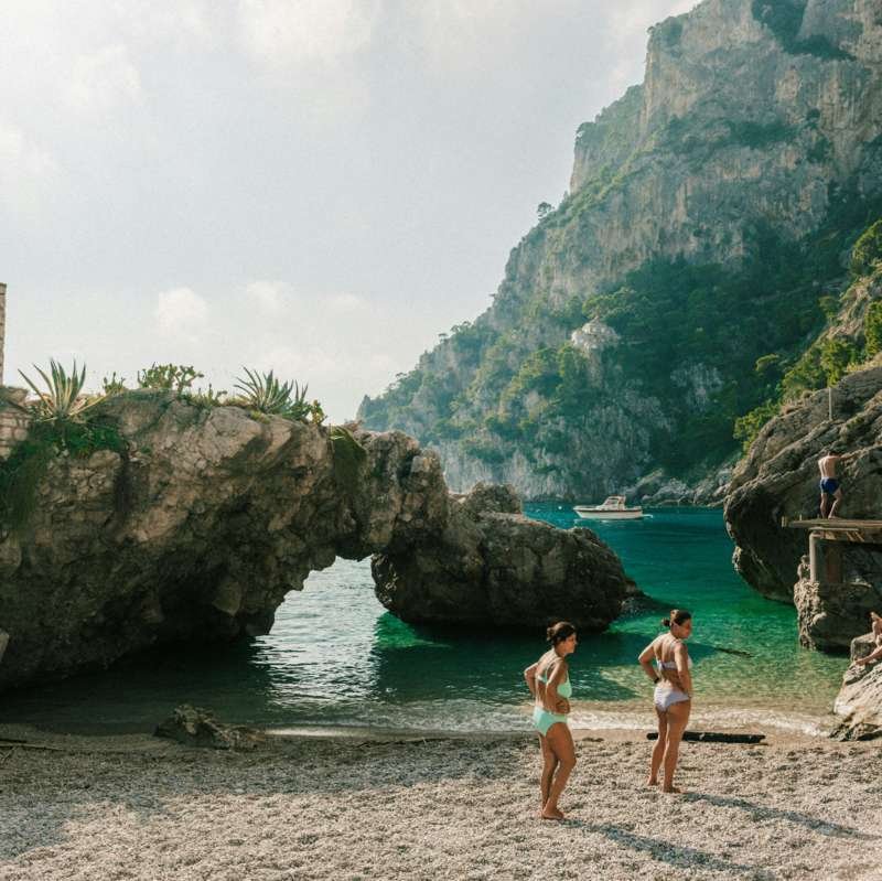 Bagnanti sulla spiaggia di ciottoli di Marina Piccola a Capri con arco di roccia e scogliere verdi